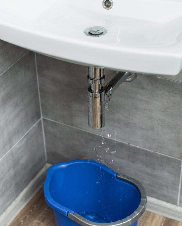 damaged-sink-pipe-with-water-drops-and-blue-bucket-2024-11-18-11-50-48-utc